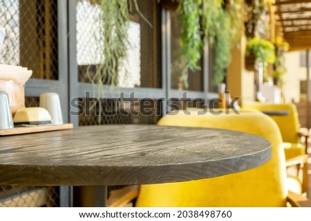 Round wooden table and cozy yellow chair at street cafe. Vacant restaurant furniture on the terrace outdoors.