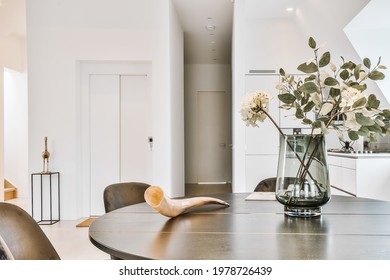 Round Wooden Table With Glass Vase Of Flowers And Decorative Horn Against White Colored Kitchen