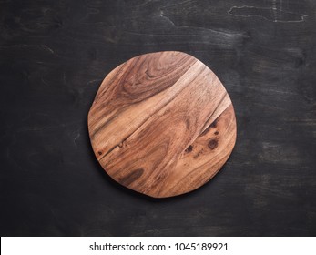 Round Wooden Tray Or Cutting Board On Black Table. Top View Of Empty Kitchen Trendy Rustic Wooden Tray Saw Cut Imitation On Black Wooden Background. Copy Space For Text. Food And Menu Background.