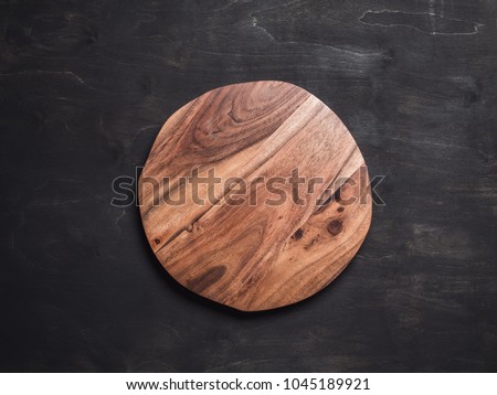 Round wooden tray or cutting board on black table. Top view of empty kitchen trendy rustic wooden tray saw cut imitation on black wooden background. Copy space for text. Food and menu background.