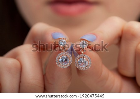 
Round zircon stone rose earrings in women's hands with colored nail polish
