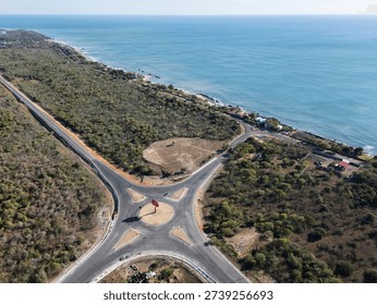 A roundabout sits at the intersection of two roads along the coast. The sea is visible at one side and trees surround the area.