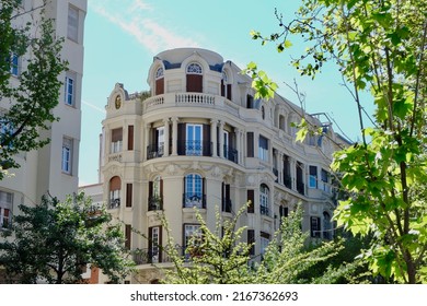 Rounded corner of elegant classical facade seen through trees, Fuencarral district, center of Madrid, Spain