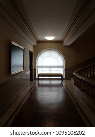 A rounded window with a bench at the end of a starcase hallway.