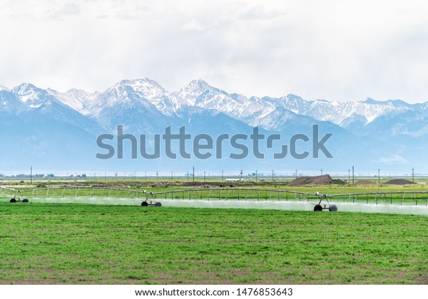 Route 285 in\
Colorado with countryside green farm near Saguache and view of\
Rocky Mountains with water\
sprayer