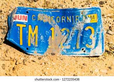 Route 66, California, USA - May 14, 2018: Detail Of Old Damaged Car Licence Plate Lost In Desert Yellow Sand On Arizona Californian Border. American Road Trip Background - Illustrative Editorial