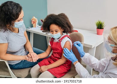 Routine Vaccinations For A Child. African American Girl And Her Mother Wearing Medical Masks While Vaccinated By A General Practitioner