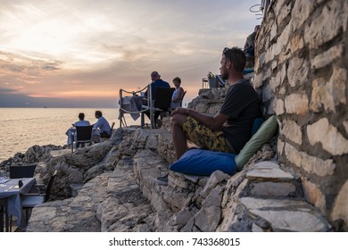 Rovinj Croatia Alongside The Adriatic Sea, People Diner Along The Ocean Watching Sunset Over The Sea By Rovinj