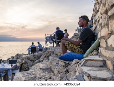 Rovinj Croatia Alongside The Adriatic Sea, People Diner Along The Ocean Watching Sunset Over The Sea By Rovinj