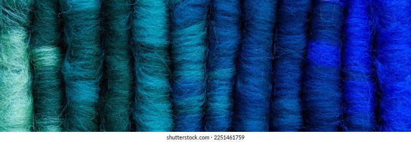 A row 12 hand  made merino wool rolags  lined up to show the colour gradient from greens to turquoise to blues  Rolags are used to spin woollen yarns  Banner format 