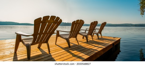 Row of Adirondack chairs -patio - deck chairs on wooden dock with sunset or sunrise -cottage life. Banner - panoramic - Powered by Shutterstock