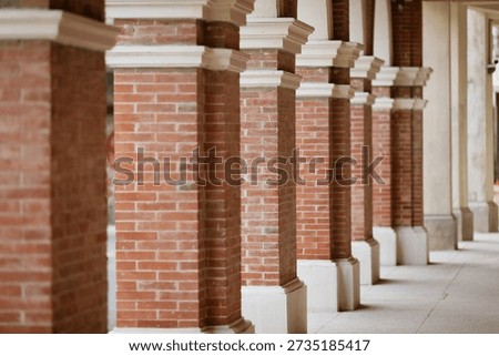 Row of aligned brick columns with white capitals creating architectural perspective down a covered colonnade or porch.