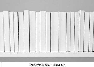 A Row Of All White Books Sit On A White Shelf In Front Of An Off White Background.