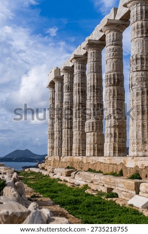 Row of ancient Doric columns of the Temple of Poseidon at Cape Sounion under a cloudy blue sky with a view of the sea and mountains
