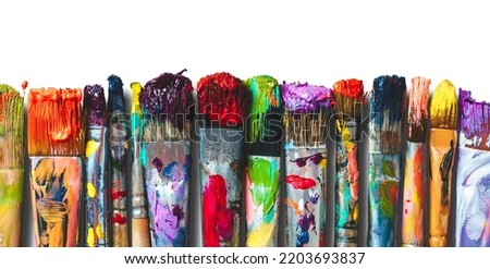 Row of artist paintbrushes closeup on white. Artistic brushes smeared with paints on white background.