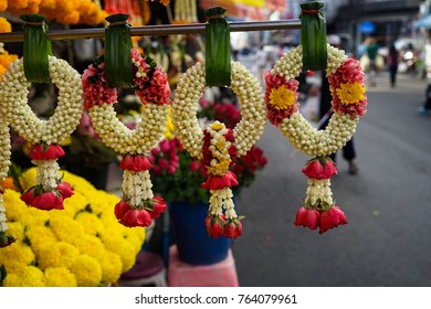 Row of beautiful fresh elaborated flower garlands in Thai style hanging on pandan leaves with local morning market background, Thailand