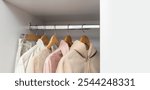 Row of beige casual clothes on the wooden hangers. White empty space for design. Concept of clothing capsule for natural lifestyle