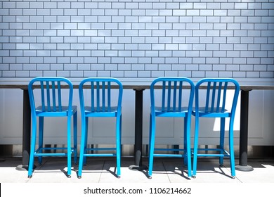 Row Of Blue Bar Stool Chairs Along A White Tile Wall, At An Outdoor Restaurant Patio, With Space For Text On Top