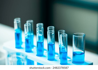 A row of blue test tubes are lined up on a white lab bench. The tubes are filled with clear liquid, and the overall mood of the image is one of scientific experimentation and discovery