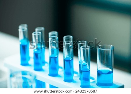 A row of blue test tubes are lined up on a white lab bench. The tubes are filled with clear liquid, and the overall mood of the image is one of scientific experimentation and discovery