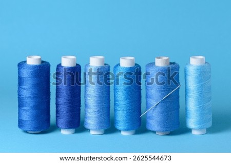Row of blue thread spools with needle aligned background with copy space for text close-up flat lay top view