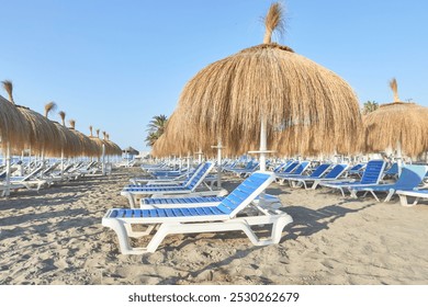 Row of blue and white sun loungers with straw parasols on the sand of a beach in Torremolinos, Malaga, Andalusia, Spain - Powered by Shutterstock