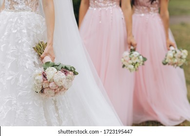 Row of bridesmaids with bouquets at wedding ceremony. Three bridesmaids holding wedding bouquets. Bride With Bridesmaids Outdoors At Wedding
