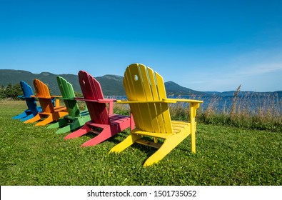 A Row of Bright and Colorful Adirondack Chairs Facing Bonne Bay on a Sunny Day in Newfoundland