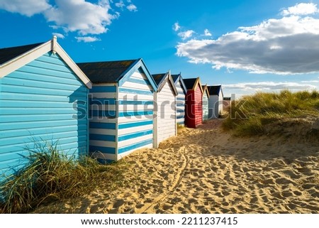 Row of brightly painted beach houses seen on golden sand by sand dunes. Located on the Suffolk coast in the UK.