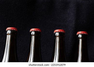 A row of brown beer bottles with red metallic caps against a dark background. Copy space above. Home beer brewing concept.