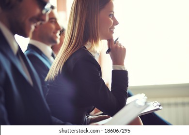 Row of business people making notes at seminar, focus on attentive young female - Powered by Shutterstock