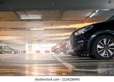 Row Of Cars In A Car Park Or Dealership. Selective Focus. Low Angle Shot. Light Glow In The Background. Dark Color Car In Foreground. Busy Parking Lot.