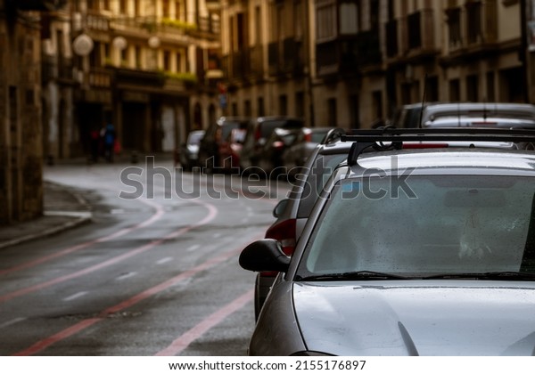 Row of cars parked along the street and old\
buildings in Europe city. Many cars parked on road in old town.\
City street in Europe. Front view of car parked outside residential\
building. City traffic.