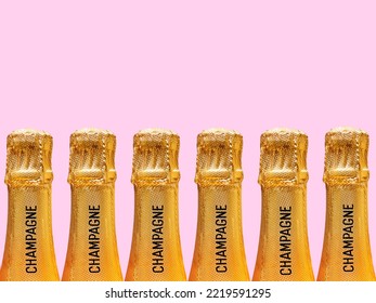Row of champagne bottles covered in gold foil stamped with the word champagne on the neck against a plain pink background. No people. Copy space. - Shutterstock ID 2219591295