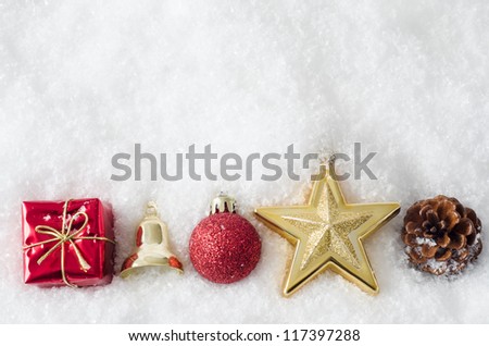 A row of Christmas ornaments, bordering bottom of frame, partially buried in white artificial snow.  Copy space above.