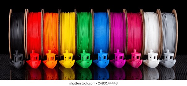 row of colorful 3d printing filament PLA material on environmentally friendly and recyclable paper cardboard spools on black carbon fiber background. modern FDM printer technology concept