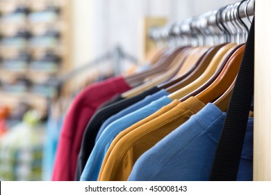 Row Of Colorful Apparel On Shoulders Hangers Of Gondola Of Retail Shop With Other Items On Background