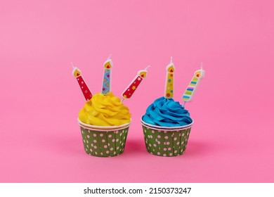 A row of colorful cupcakes with candles on a pink background.