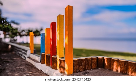 A row of colorful wooden posts are lined up on a beach. The colors are red, yellow, and blue. The scene is peaceful and serene, with the ocean in the background - Powered by Shutterstock