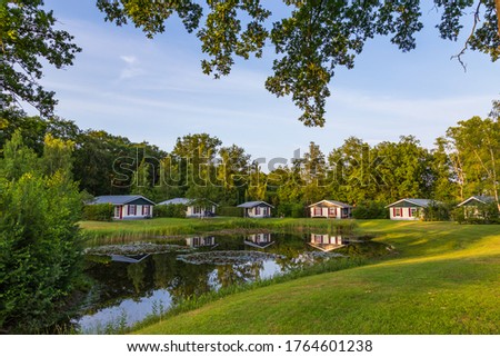 Row of colorful wooden vacation home reflected in a pond at recreation park in the middle of nature in the Netherlands