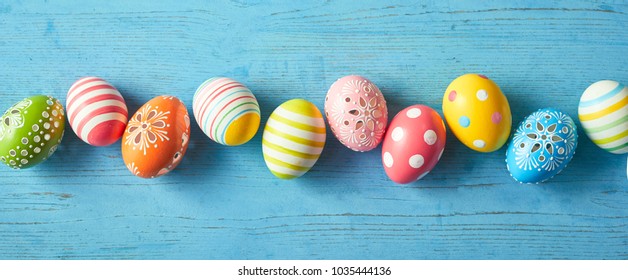 Row of colorfully painted Easter eggs on blue wooden background, wide angled image.