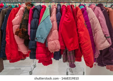 Row Of Colourful Red And Pink Tone Of Kid Winter Jackets Hang On Aluminium Hanger Clothes Rack In Retail Fashion Store Or Second Hand Outlet Shop.