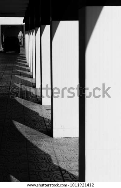 Row of columns with\
high contrast shadows on street building. Vertical pattern. Black\
and white photography