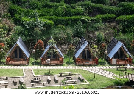 A row of comfortable and modern triangular glamping tents are located amidst green natural surroundings.
