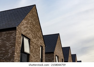 Row of contemporary brick built new build houses with front facing gables and grey slate tiled roofs against a textured sky
