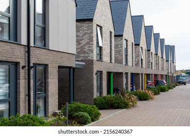 Row of contemporary new build terraced brick townhouses with grey slate roofs, coloured pillars and parking bays