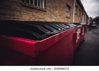 row of covered garbage bins along a brick wall in a back alley