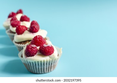 A row of cupcakes with white cream and raspberries on a blue background sharpness in the foreground. Sweet homemade cupcakes on a colored background are a place for text.