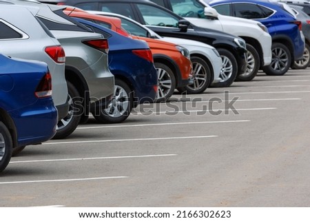 row of different color cars on asphalt parking lot at cloudy summer day with selective focus
