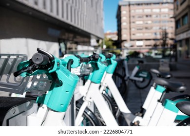 A row of e-bikes are parked in a row at a dock station in a city. It is a sunny day in Spain. Ecological concept.
